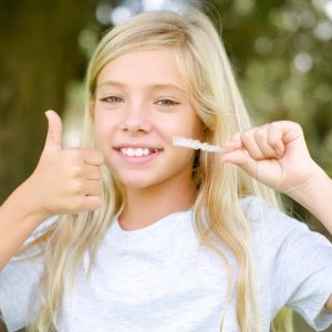 Teen girl holding up clear aligners and giving thumbs-up