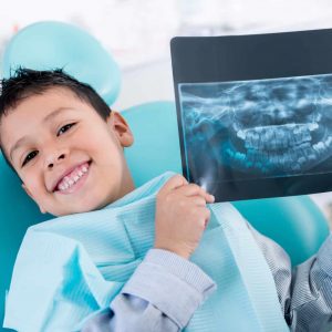 Young boy sitting in dentist chair holding up an x-ray