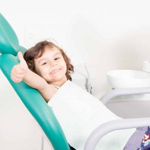 Young girl in dentist chair smiling and giving a thumbs-up